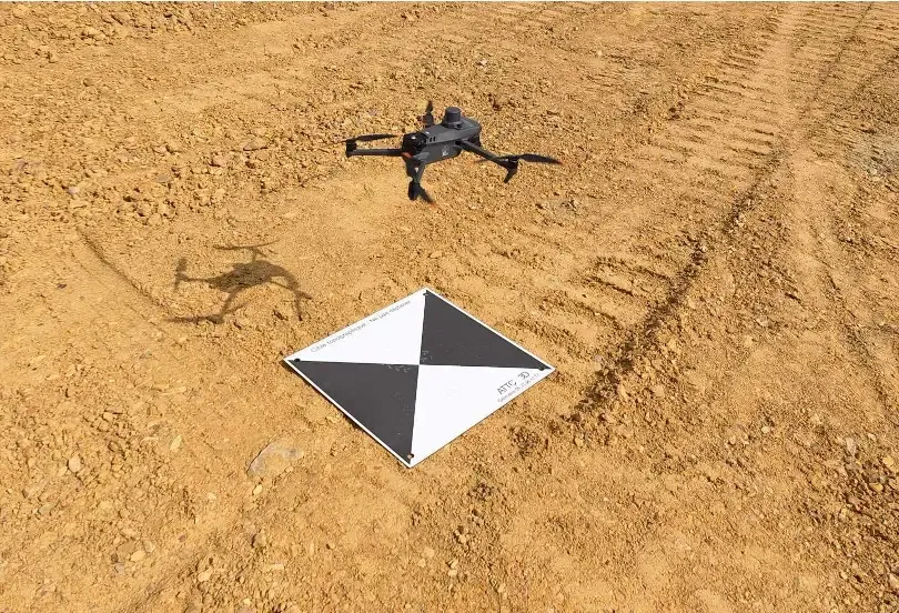 Drone DJI posé sur un terrain sablonneux près d’une cible de calage